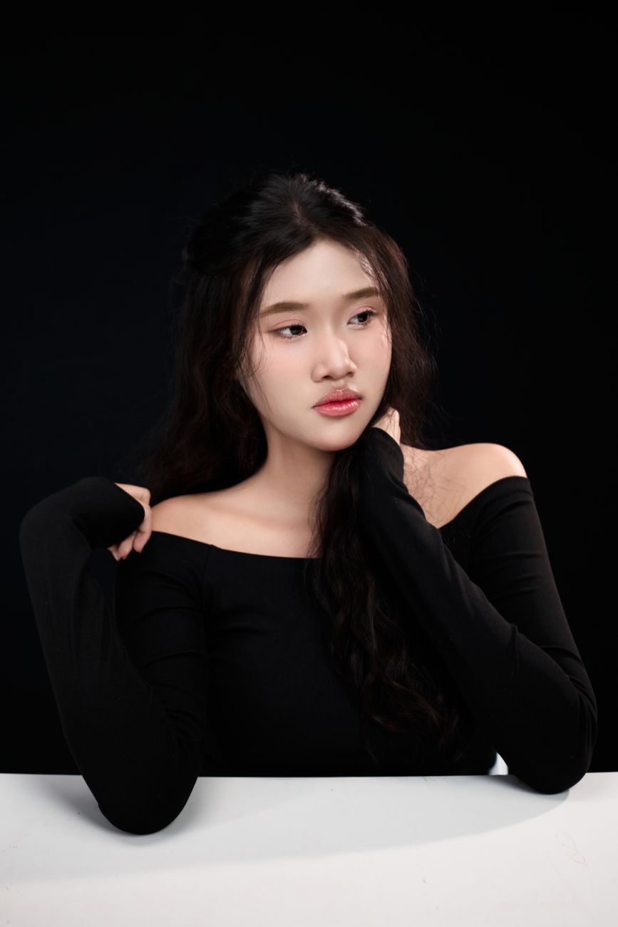 A young woman in a black outfit poses gracefully against a dark background.