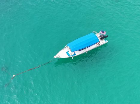 Top view of a boat with a blue canopy anchored in crystal clear turquoise sea, ideal for serene travel themes.