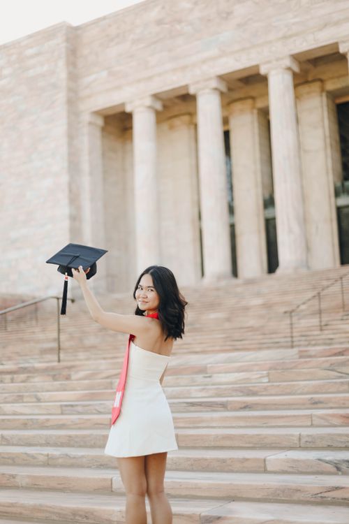 Free Young woman celebrates graduation with cap and gown on university steps. Stock Photo
