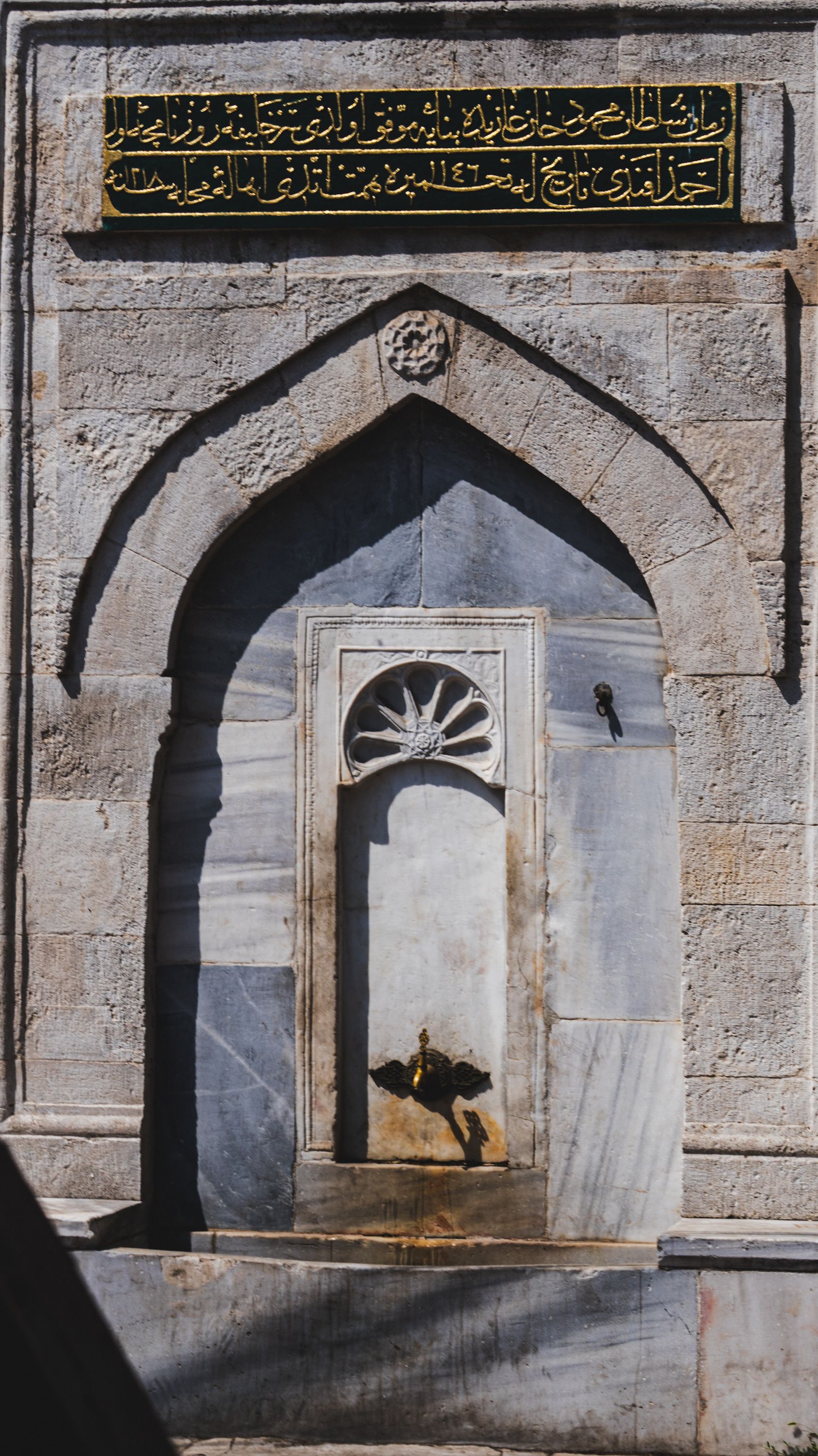 Ancient stone fountain adorned with Arabic calligraphy in a historic setting. Perfect for cultural themes.