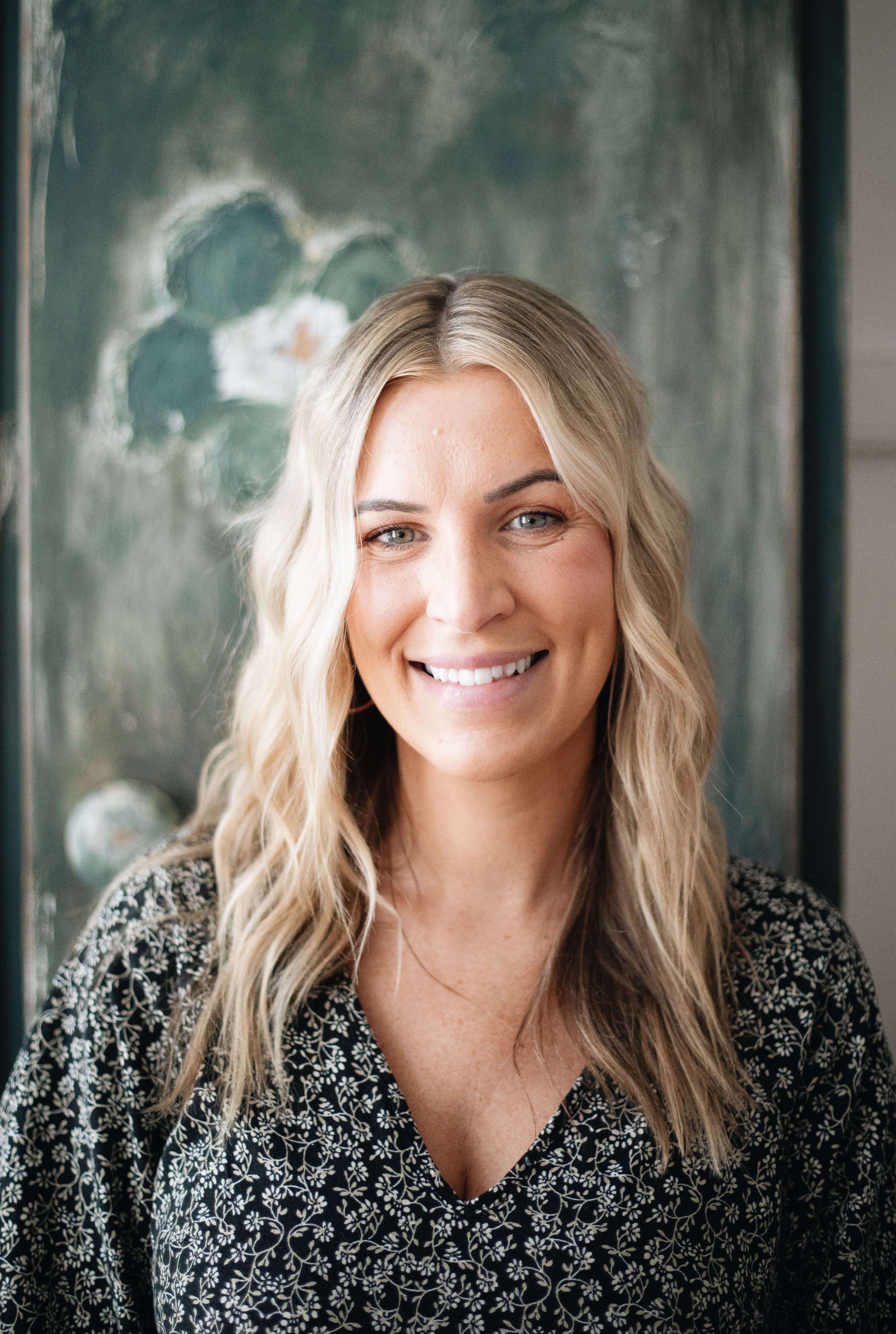 A natural light portrait of a smiling woman with wavy blonde hair for professional branding.