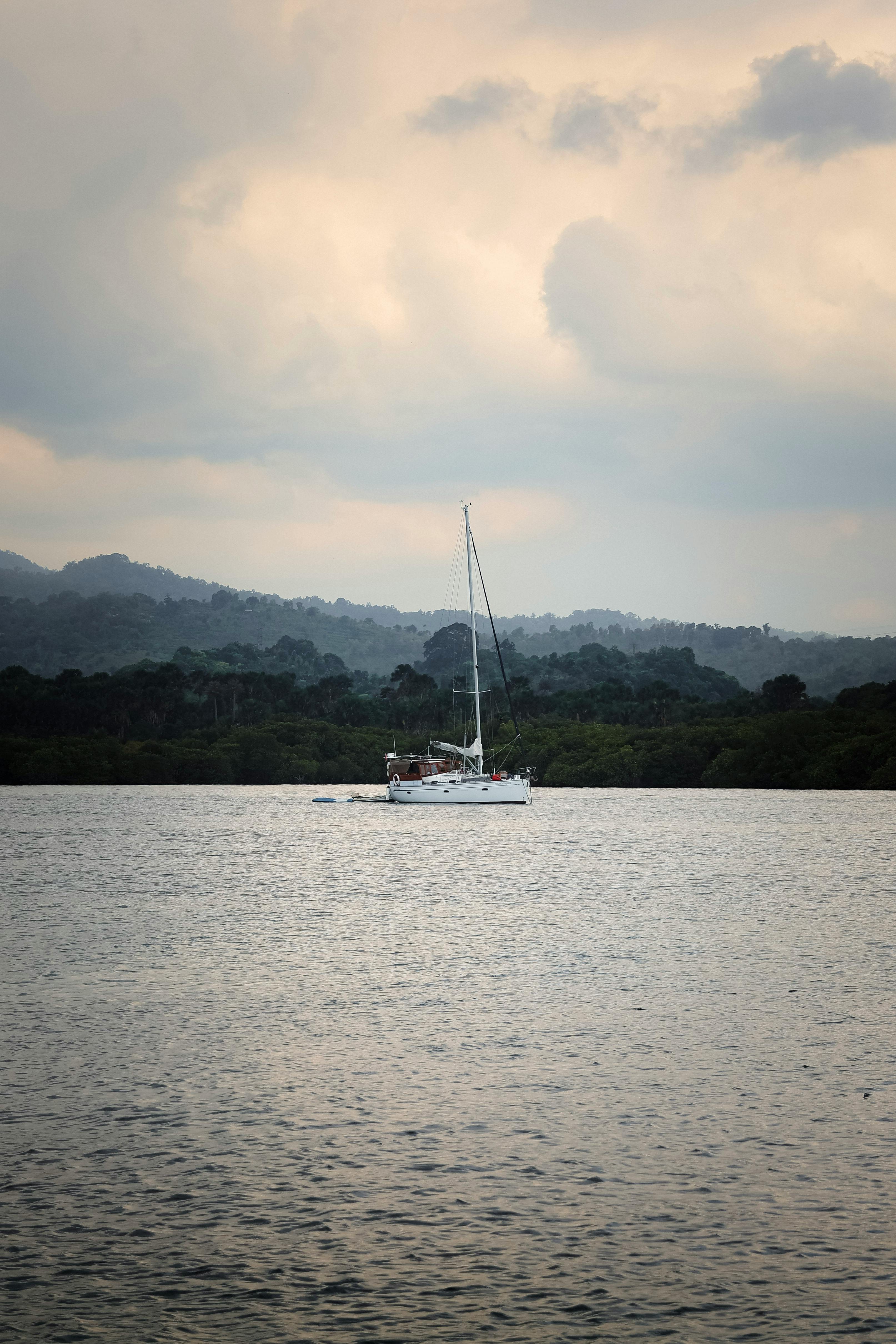Sailboat drifting peacefully on Bali's waters with lush greenery and cloudy skies in the background.