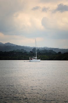 Sailboat drifting peacefully on Bali's waters with lush greenery and cloudy skies in the background.