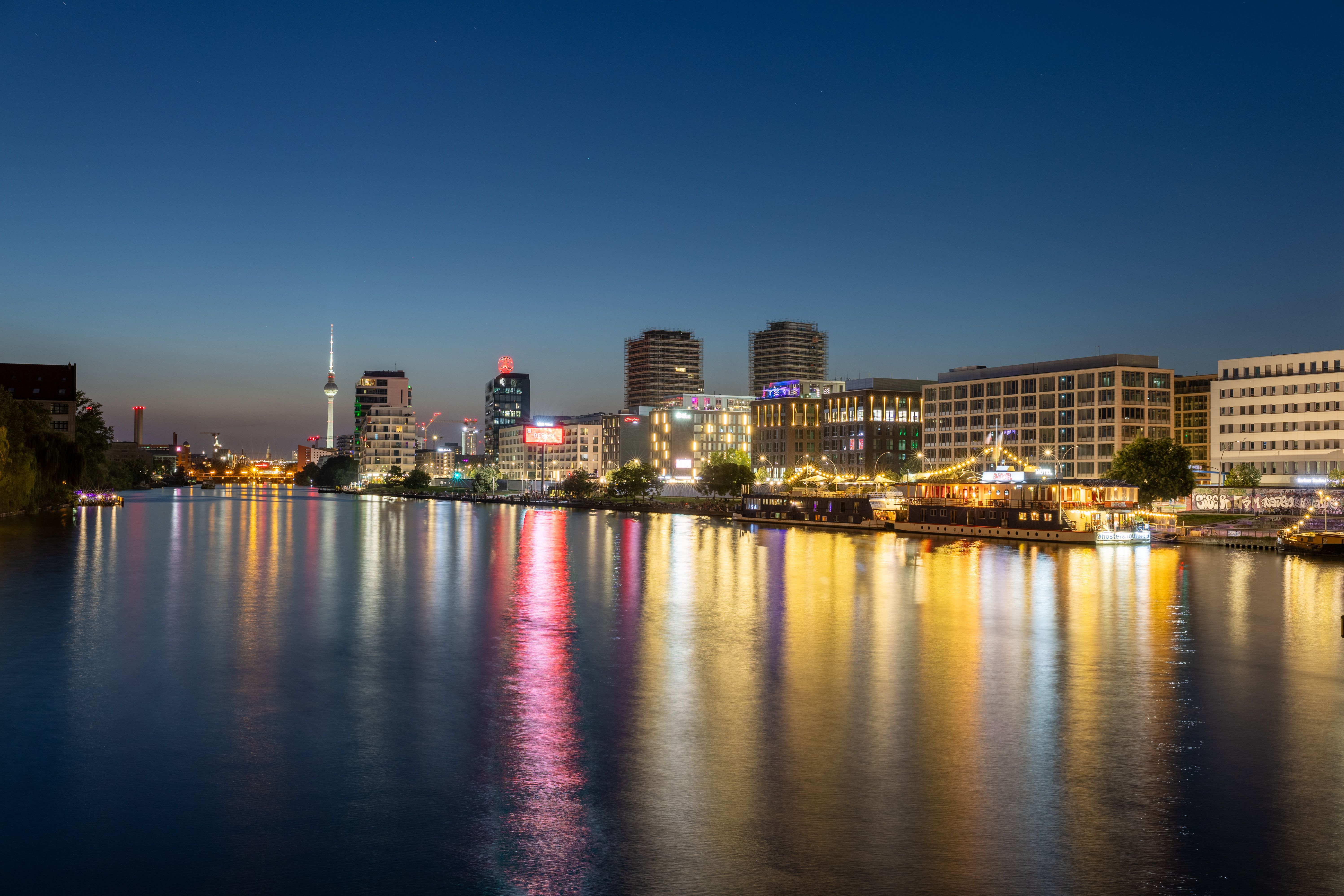 Illuminated Berlin cityscape reflecting on the Spree River during twilight.
