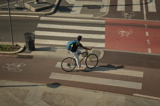 A cyclist with a backpack rides across a zebra crossing in a city intersection with bike lanes.