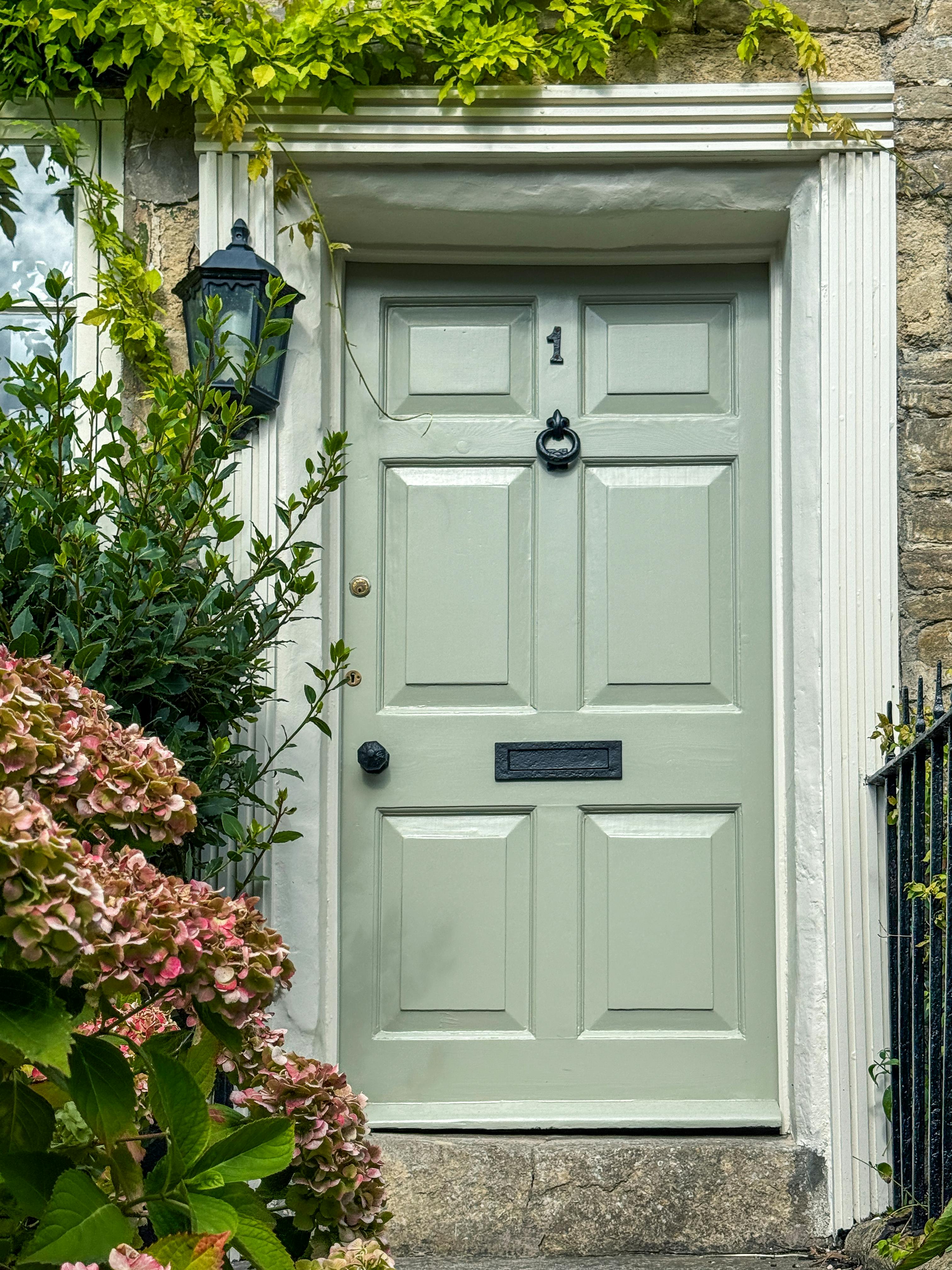 Pastel green door of an English cottage framed by hydrangeas, showcasing classic British architecture in Wiltshire, UK.