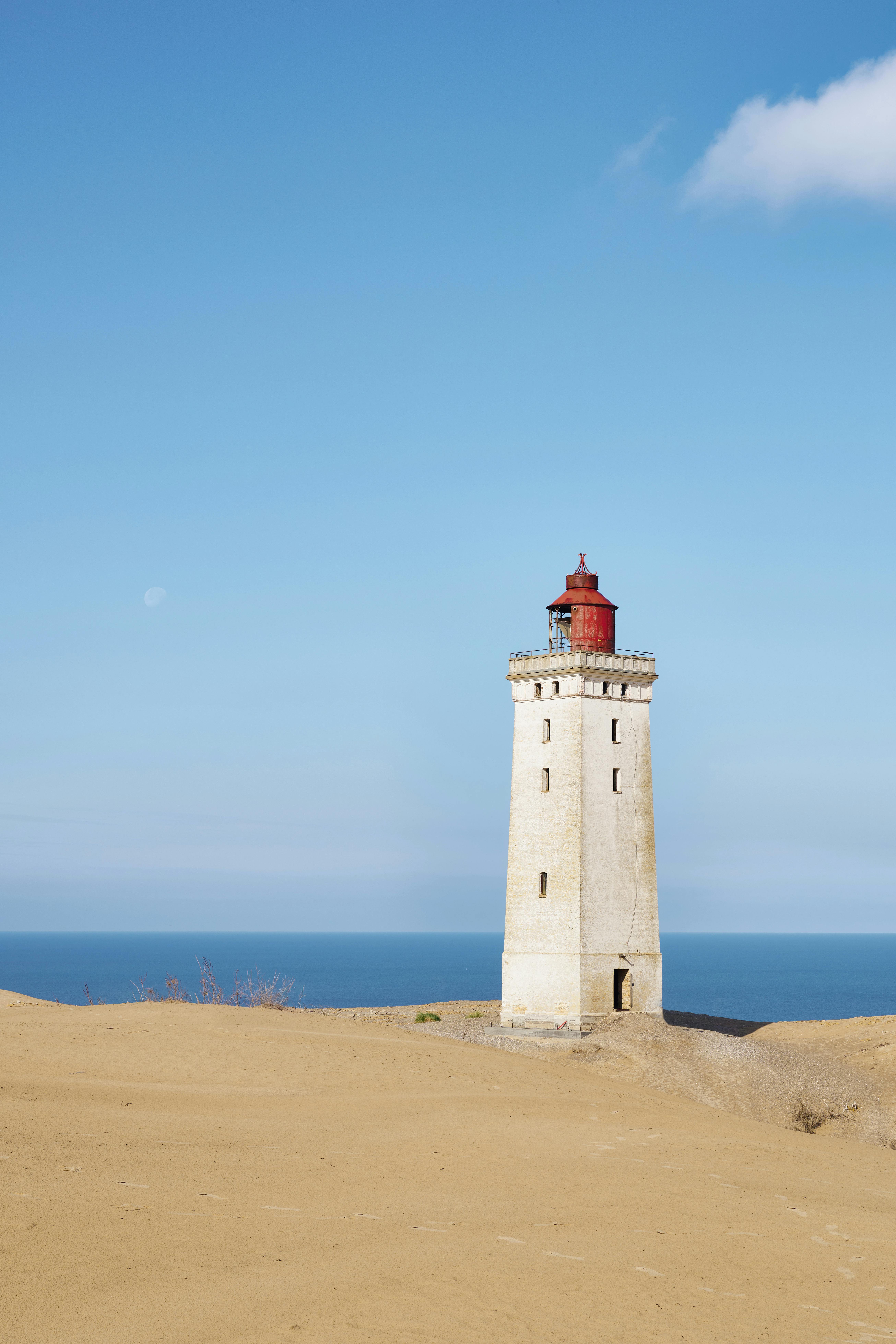 The Rubjerg Knude Lighthouse standing alone against a clear blue sky and sea in Løkken, Denmark.