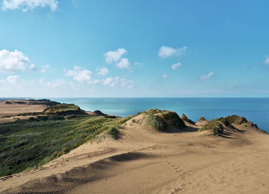 Tranquil view of sandy dunes and ocean at Løkken, Denmark on a sunny day.