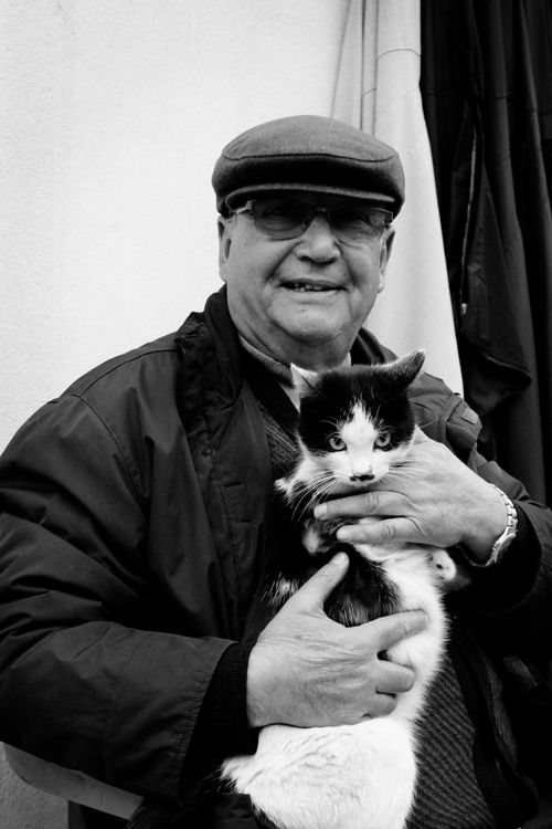 Free Elderly man joyfully holds black and white cat in candid outdoor portrait. Stock Photo