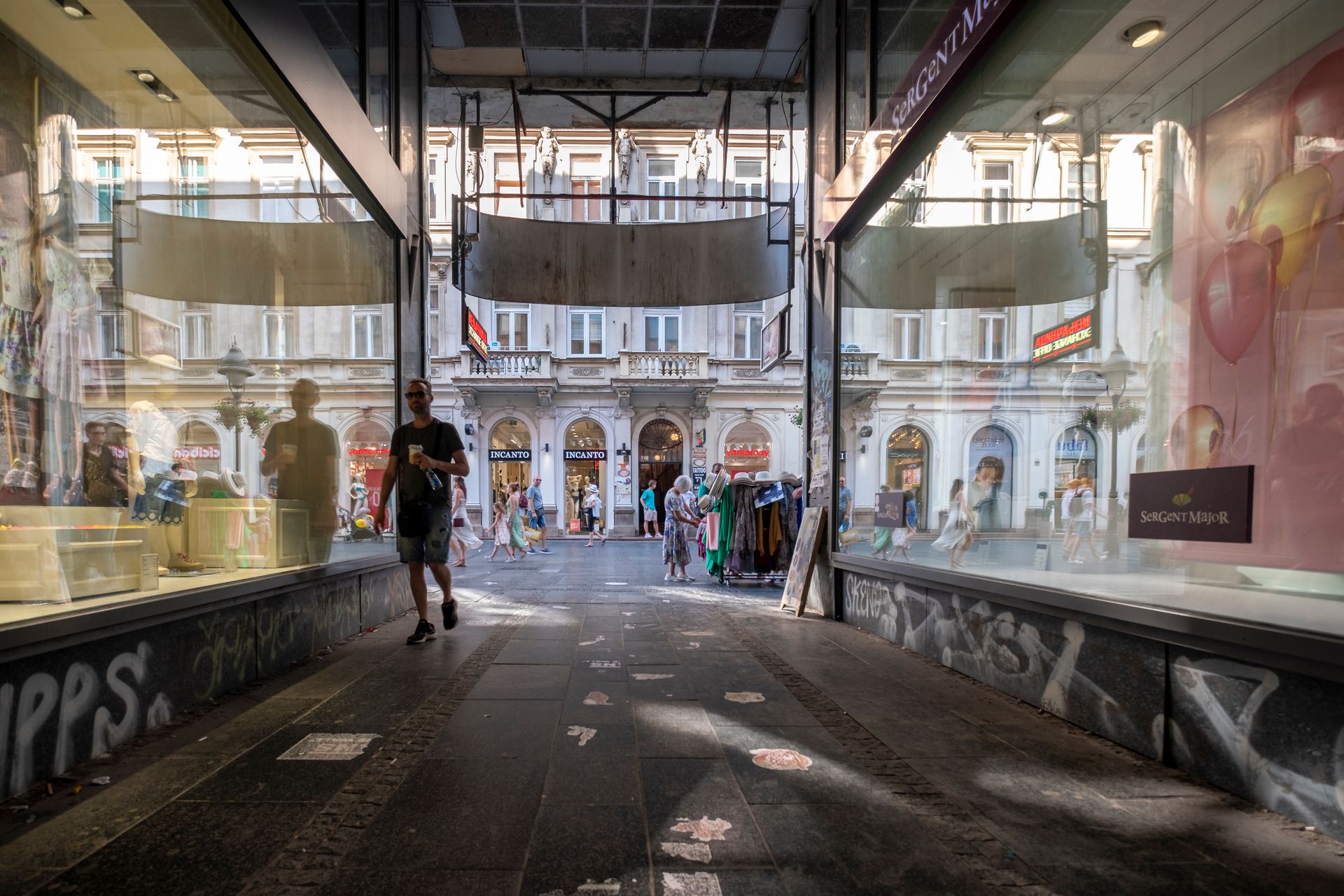 Pedestrians walking through a shopping street in Belgrade with glass reflections and historic architecture.