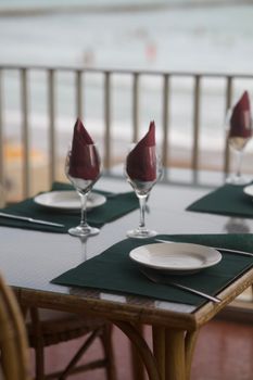Elegant dining table with wine glasses and napkins on a seaside patio.
