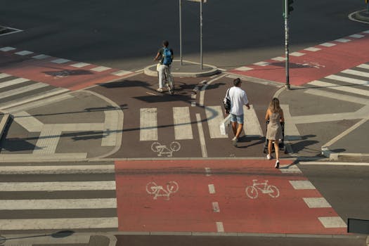A cyclist and pedestrians crossing a city intersection with marked bike lanes in Milan.