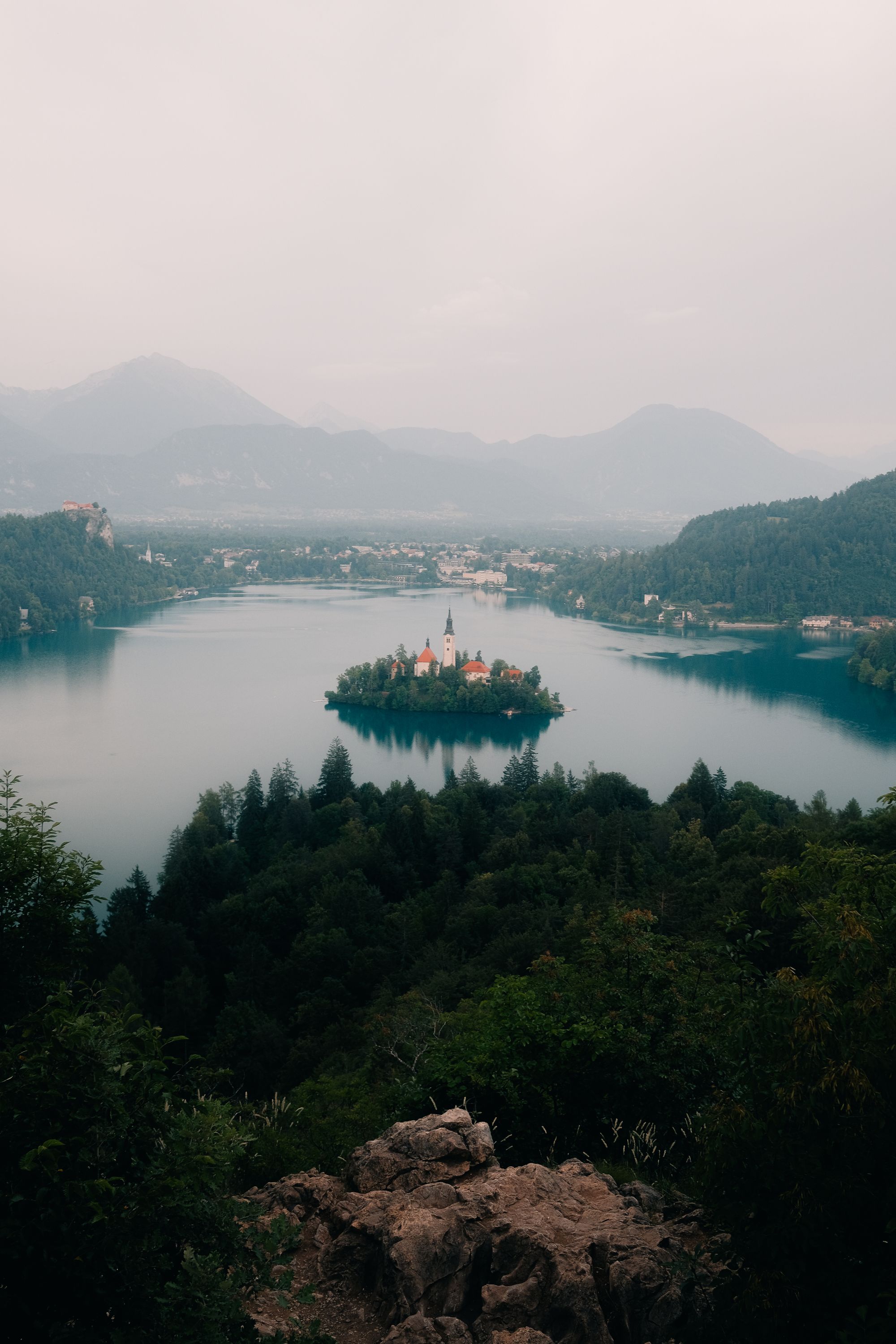 Lake Bled island seen from a forested viewpoint on a misty day