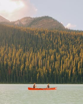 Canoe with two people on a serene lake surrounded by mountains and forest in Banff, Alberta.