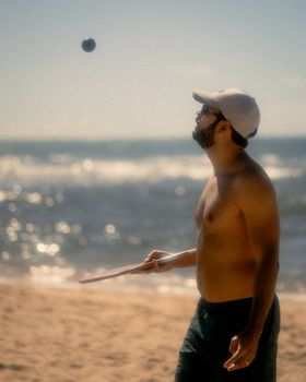 Adult playing paddle ball at the beach under bright sun, enjoying summer leisure.