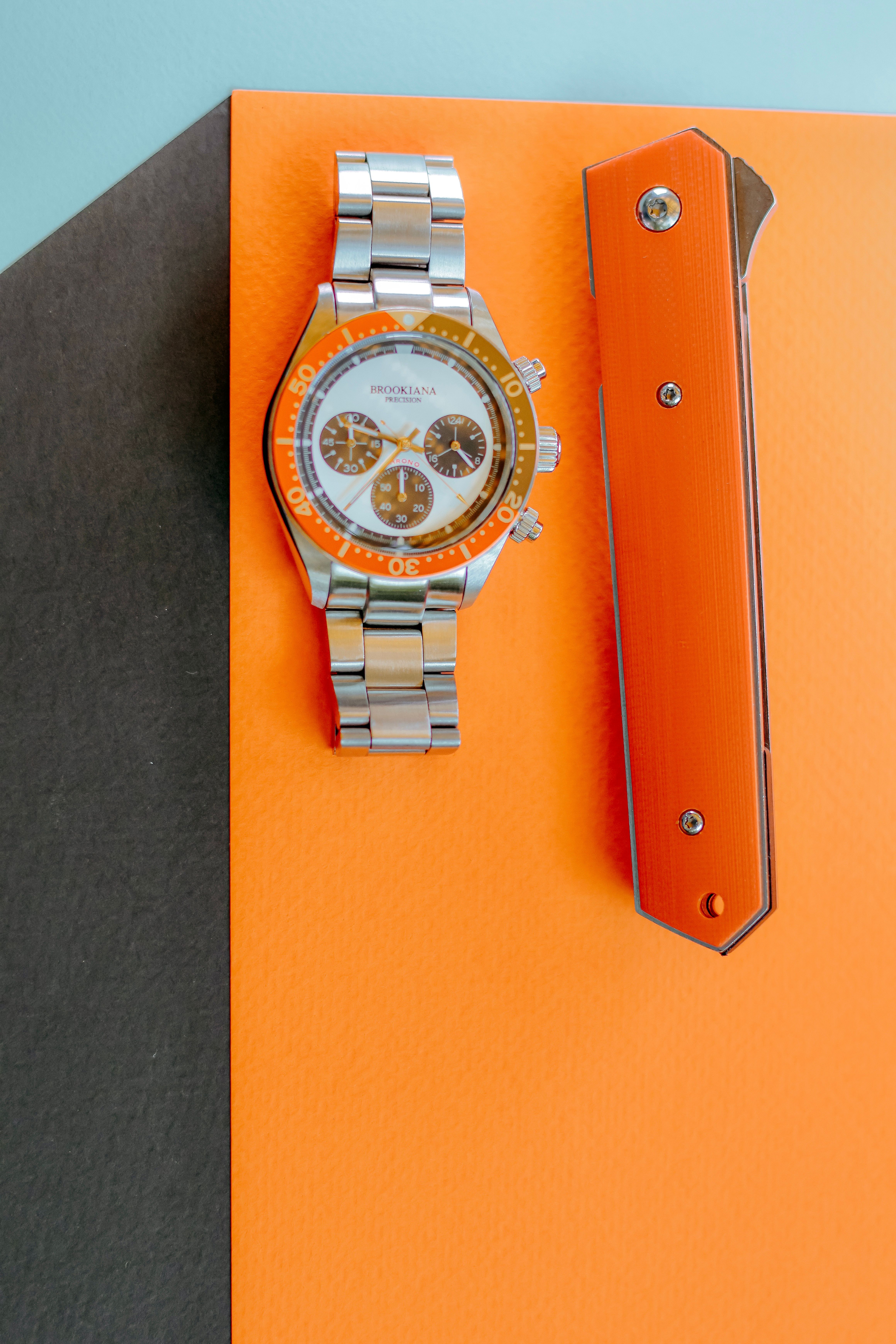High-quality image of a luxury watch and knife on an orange and blue background.