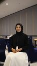 A smiling businesswoman wearing a hijab, seated indoors, exuding professionalism.
