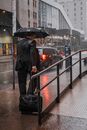一名商人撑着伞，提着行李走在城市的下雨街道上