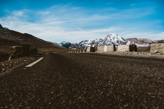 Low angle view of an empty road leading towards snow-capped mountains under a clear sky.