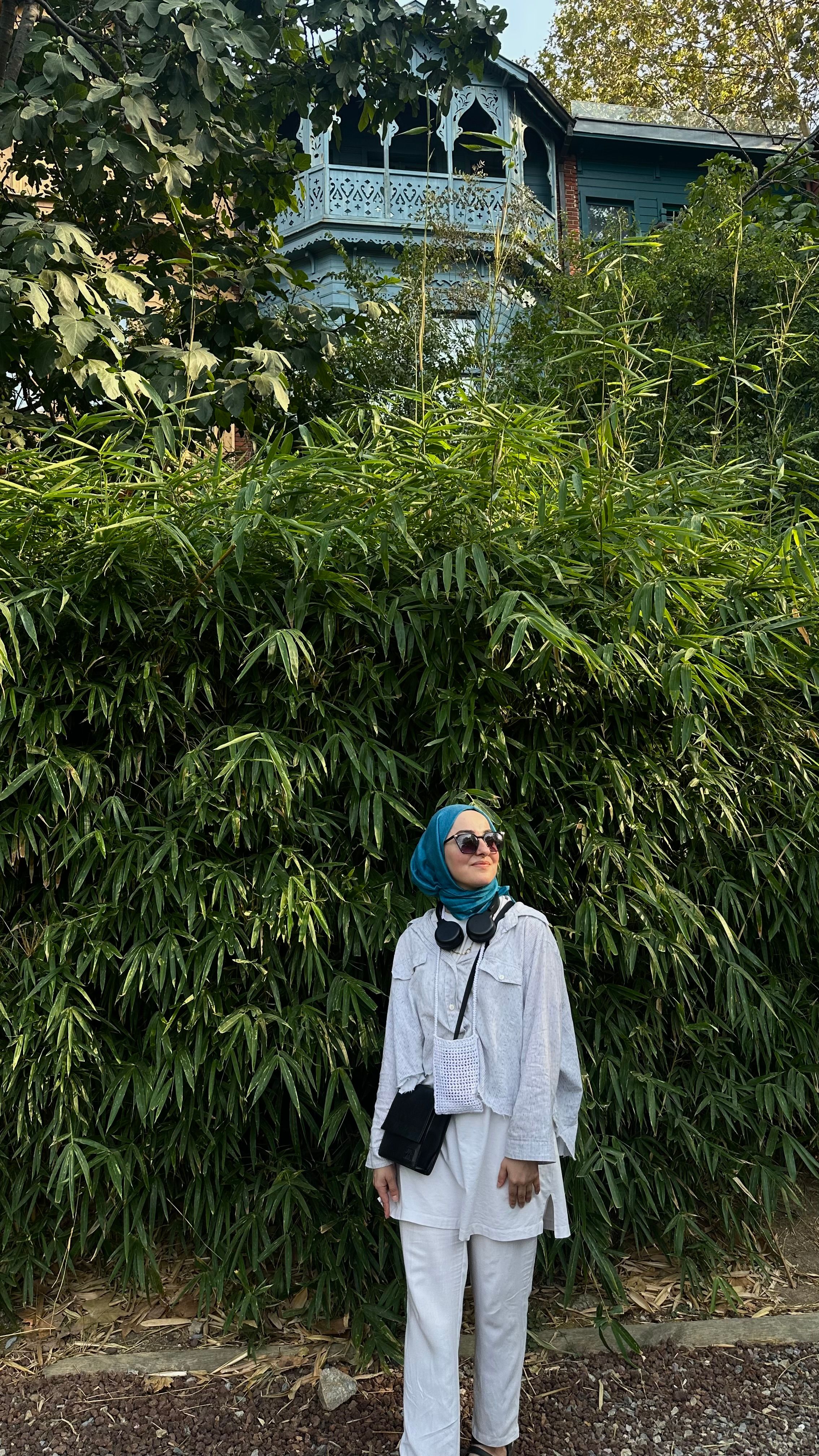 Stylish woman in white outfit with headphones standing in front of lush bamboo.