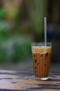 A glass of iced coffee on a wooden table, perfect for a summer day outdoors.