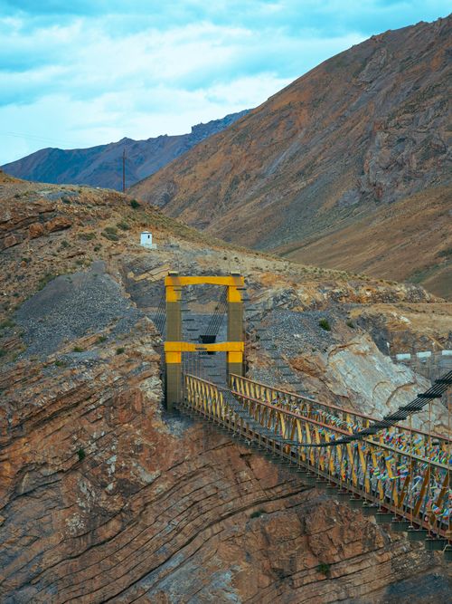 Free Dramatic view of a suspension bridge in rocky canyon with mountains and blue sky. Stock Photo