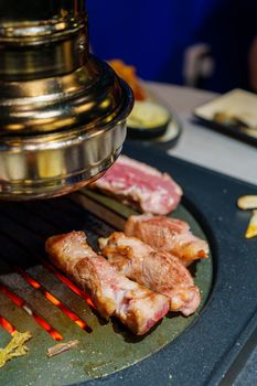 Sizzling meat on a Korean barbecue grill with a traditional exhaust hood overhead.