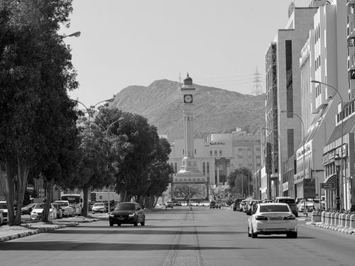Free Black and white photo of a street in Taif with a view of the clock tower and surrounding mountains. Stock Photo