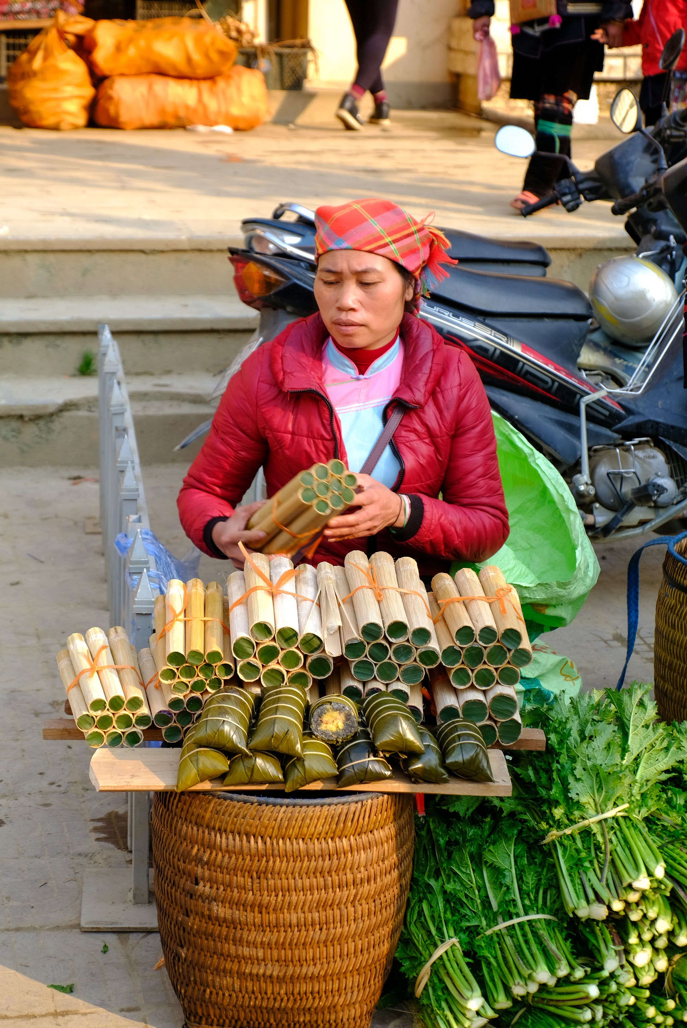 A vendor in Lào Cai, Vietnam selling traditional bamboo rice bundles outdoors at a local market.