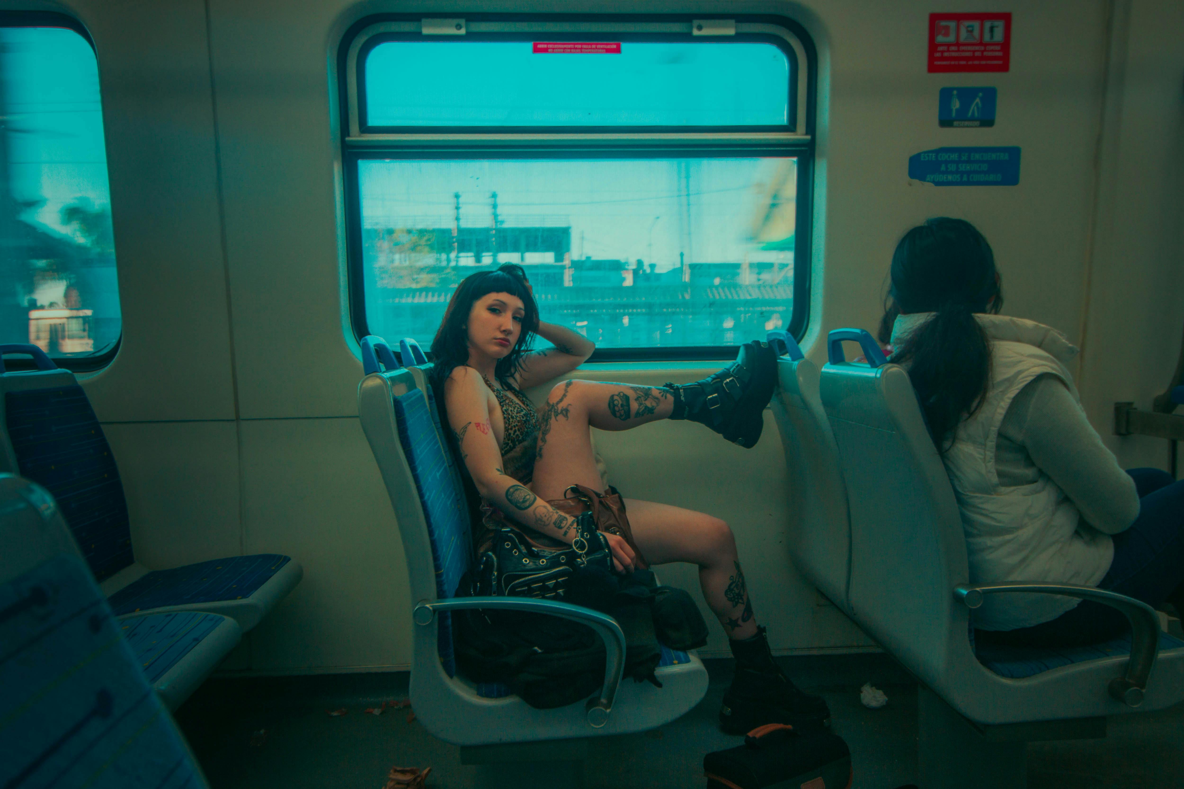 A woman with tattoos and punk attire relaxes on a train in Argentina, exuding bold style.