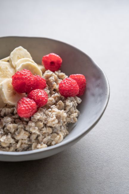 A bowl of thick protein oatmeal topped with sliced banana, a swirl of peanut butter, and a sprinkle of chopped almonds, with a spoon resting on the rim.