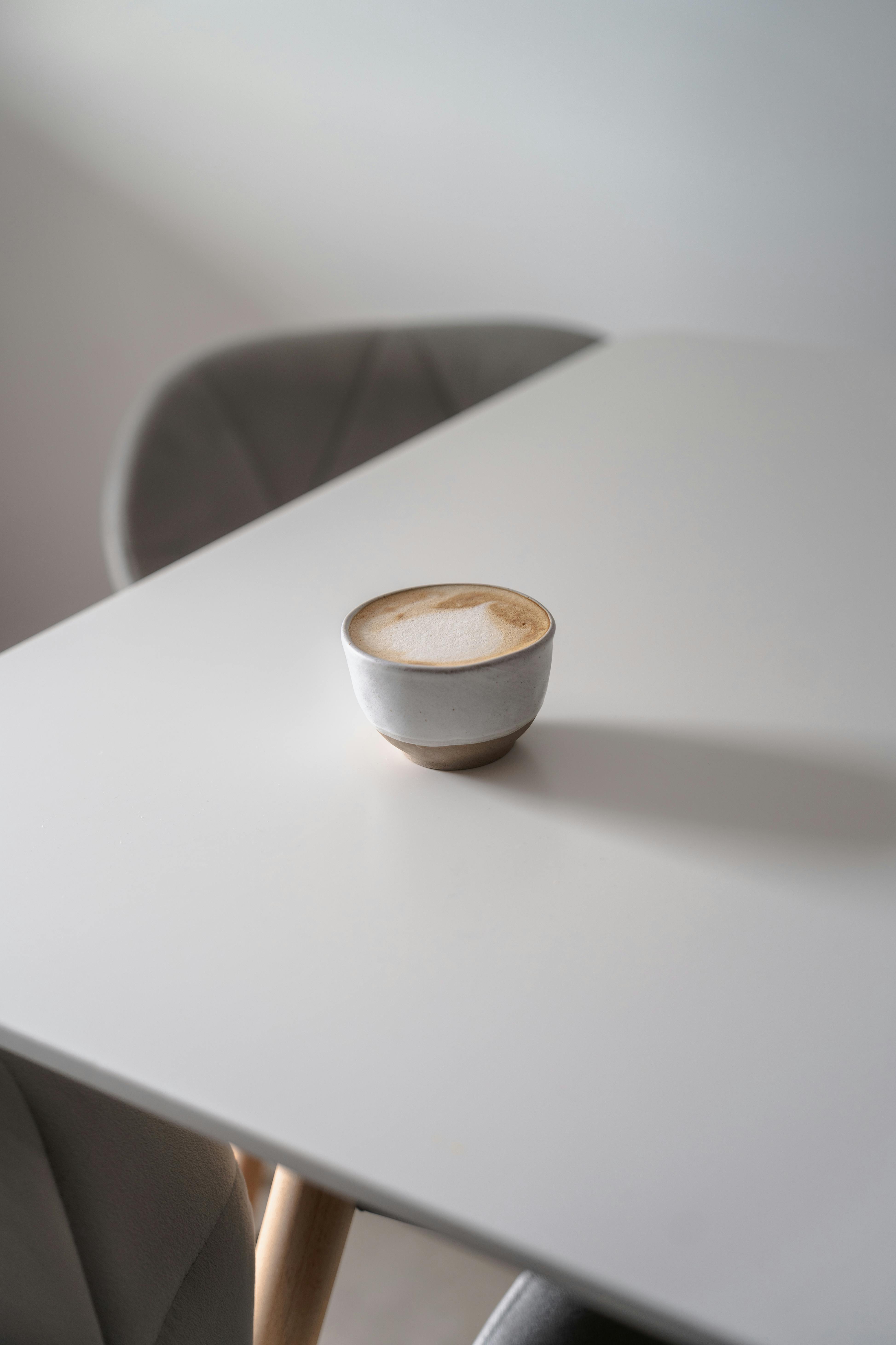 A serene scene of a coffee cup on a white table with soft natural lighting.