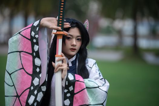 Portrait of a person in Japanese costume holding a sword in an outdoor park setting.
