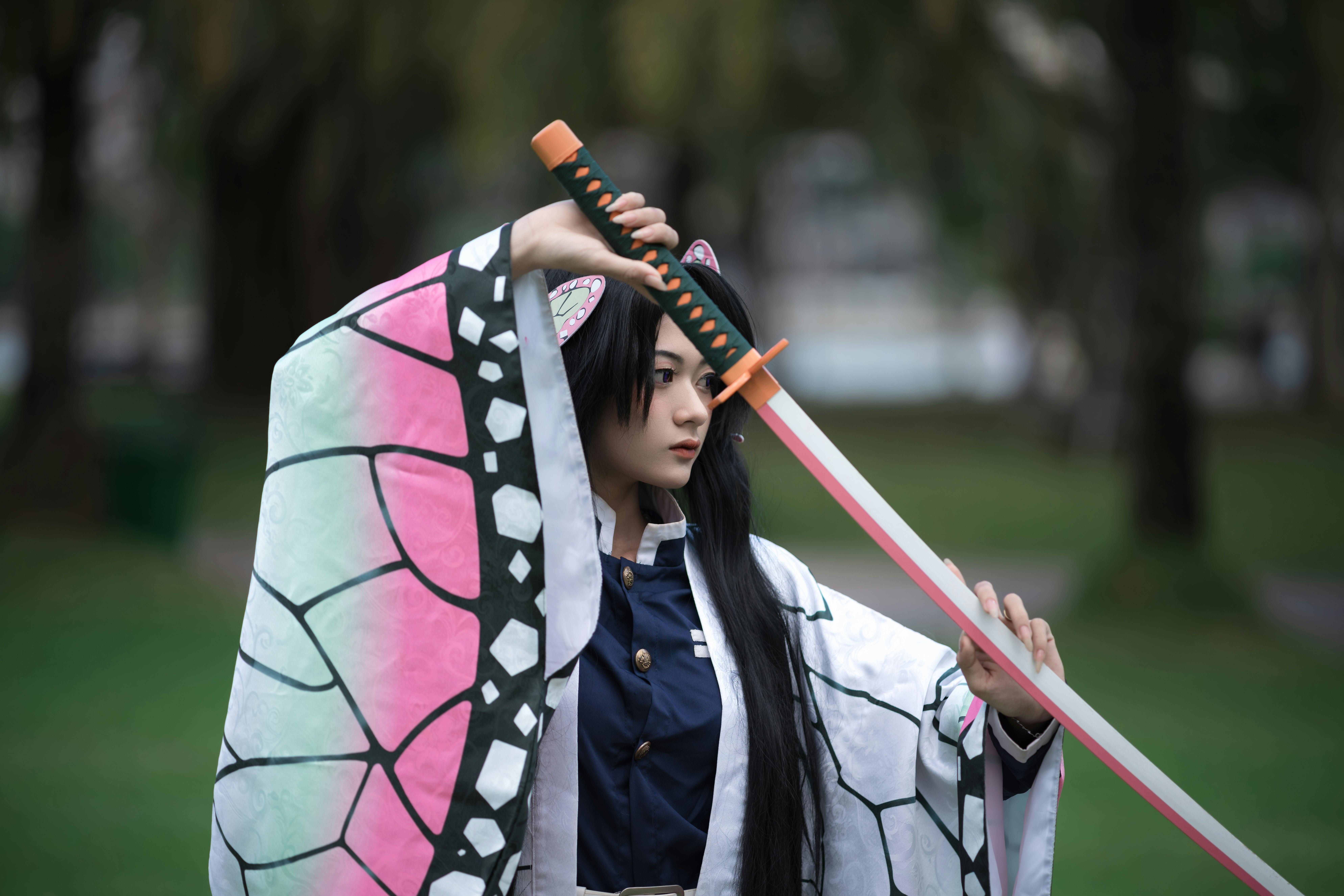 Anime character cosplay with a sword in a park, showcasing detailed costume design outdoors.