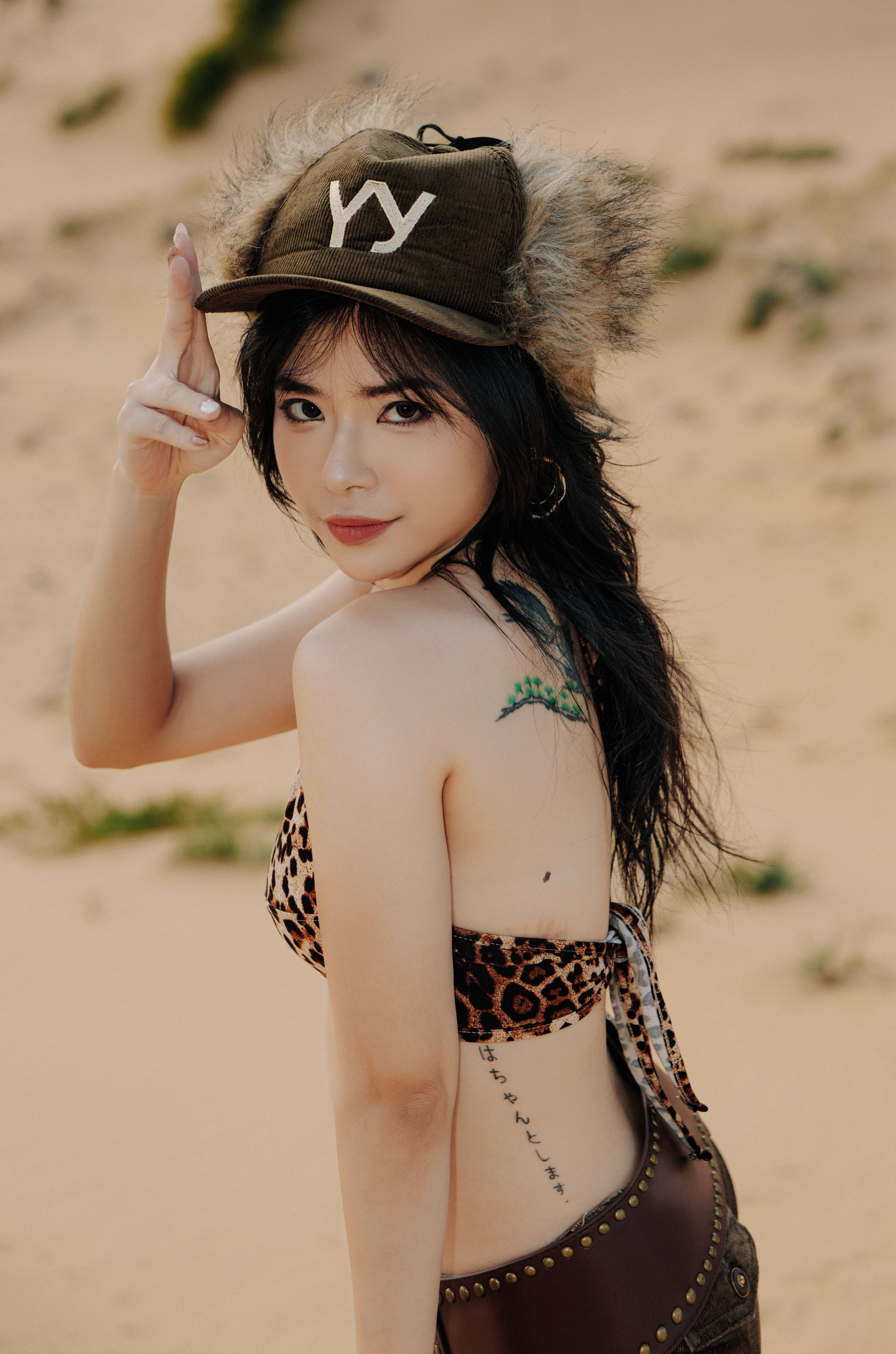 Woman in a fur hat striking a pose in a desert landscape, showcasing style and confidence.