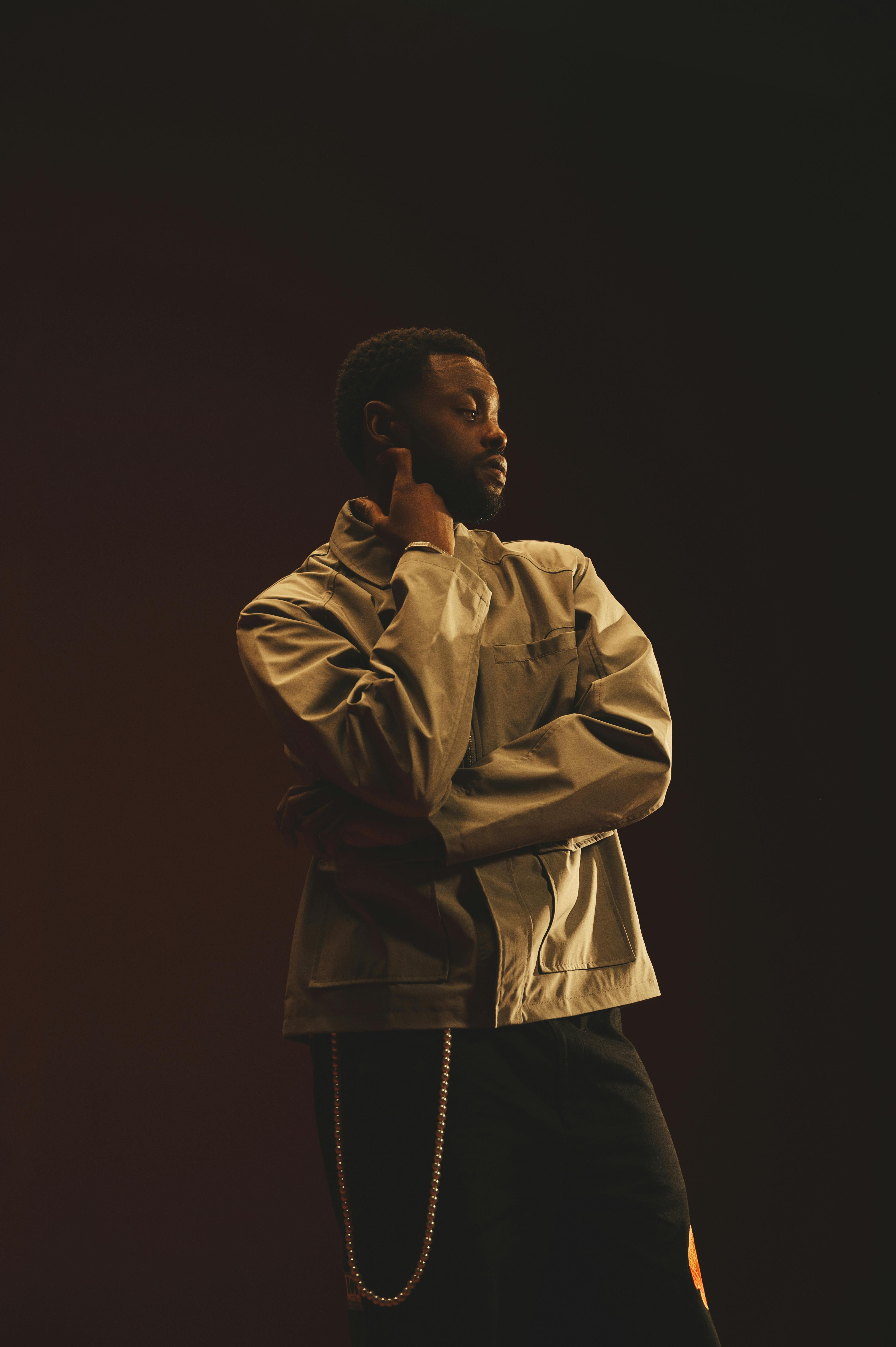 Artistic portrait of a young black man in stylish attire posing against a dark background.
