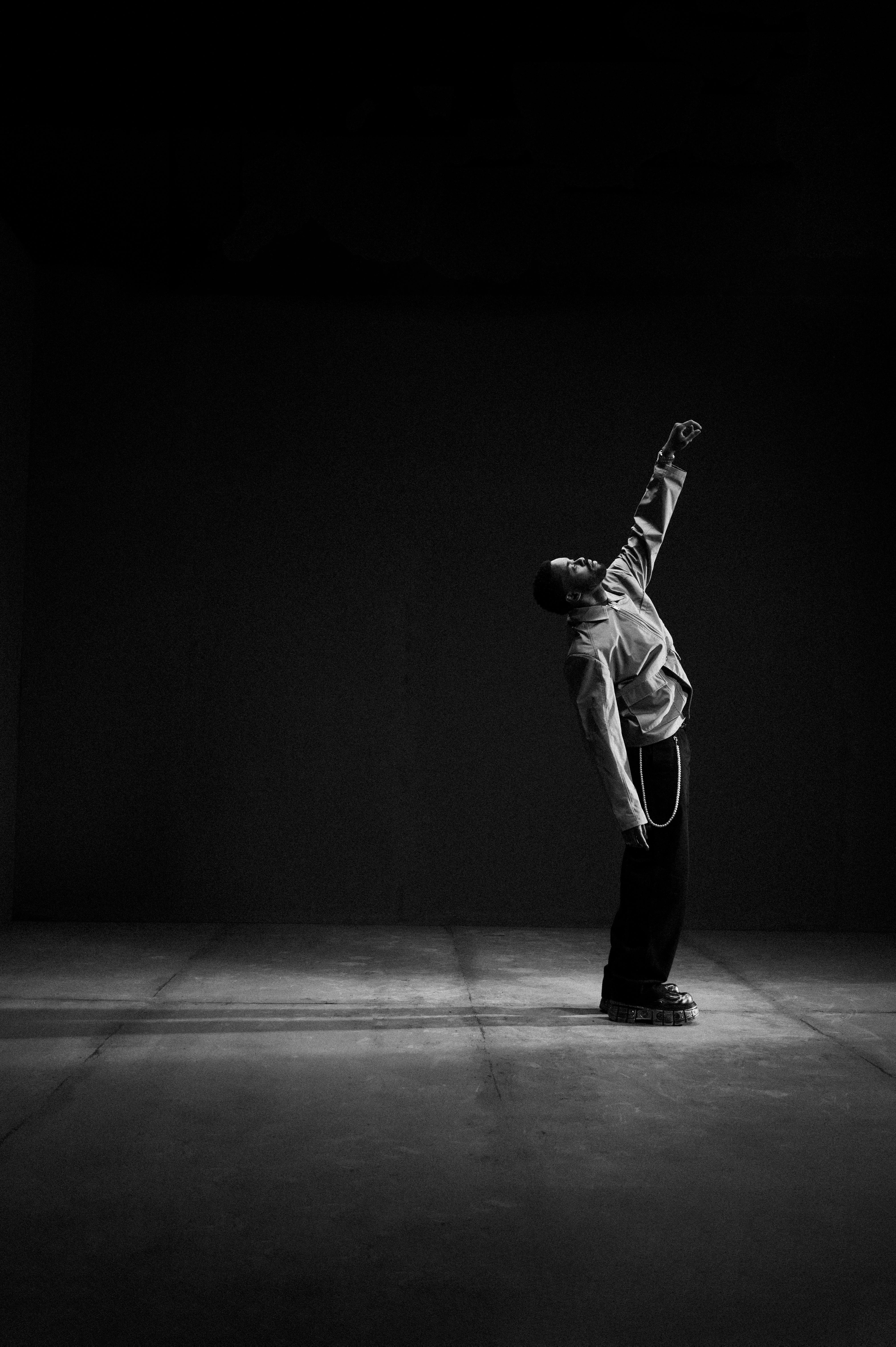 Engaging black and white portrait of a man in a striking pose under dramatic lighting.