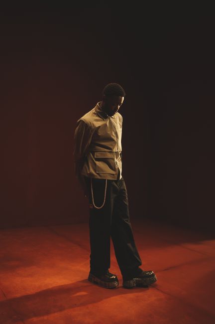 Stylish male posing in a dramatic light, wearing fashionable attire in a dimly lit studio.