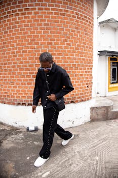 Stylish man in black outfit against a rustic brick wall, embodying urban fashion.