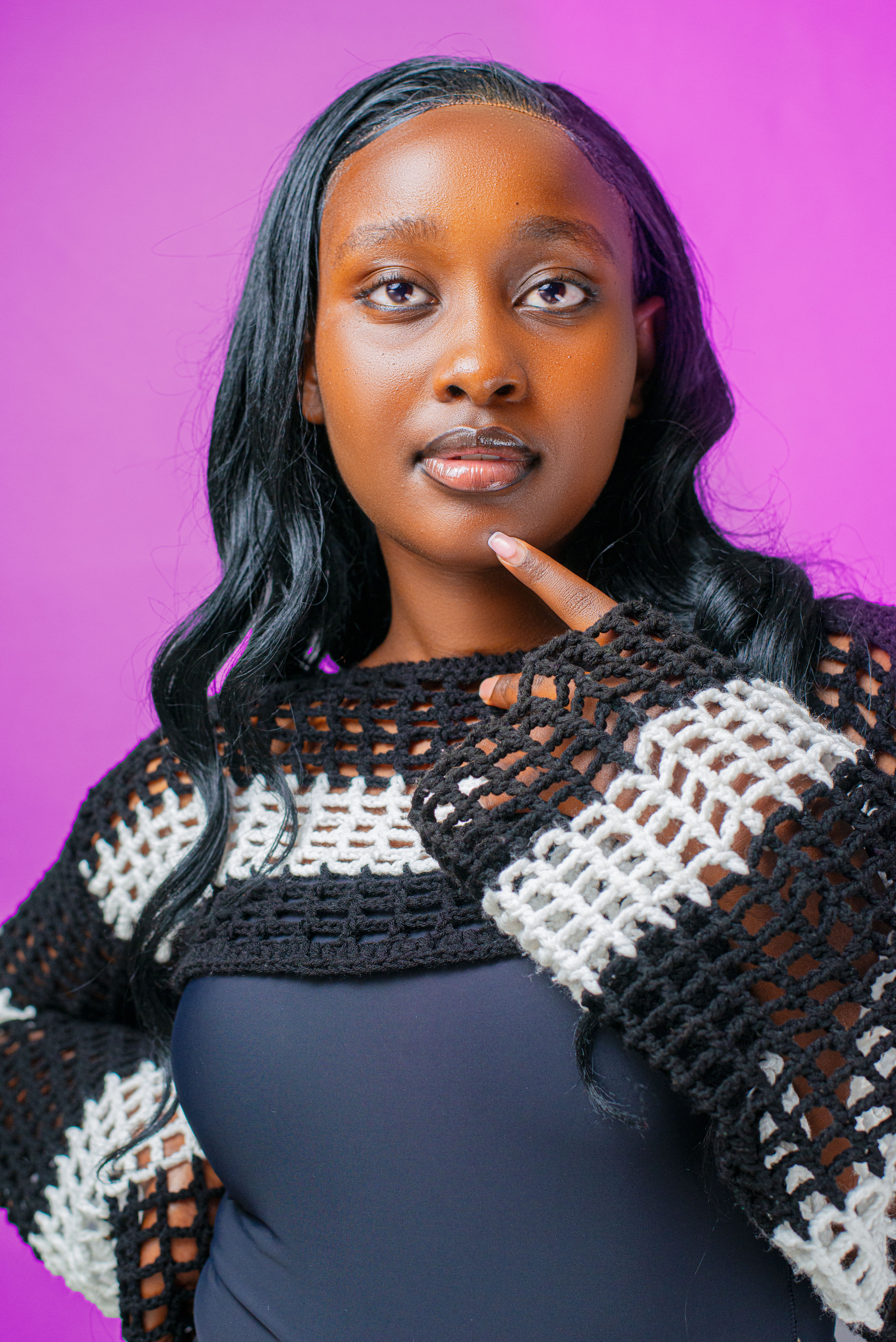 Confident woman in a black and white crocheted sweater against a purple background.