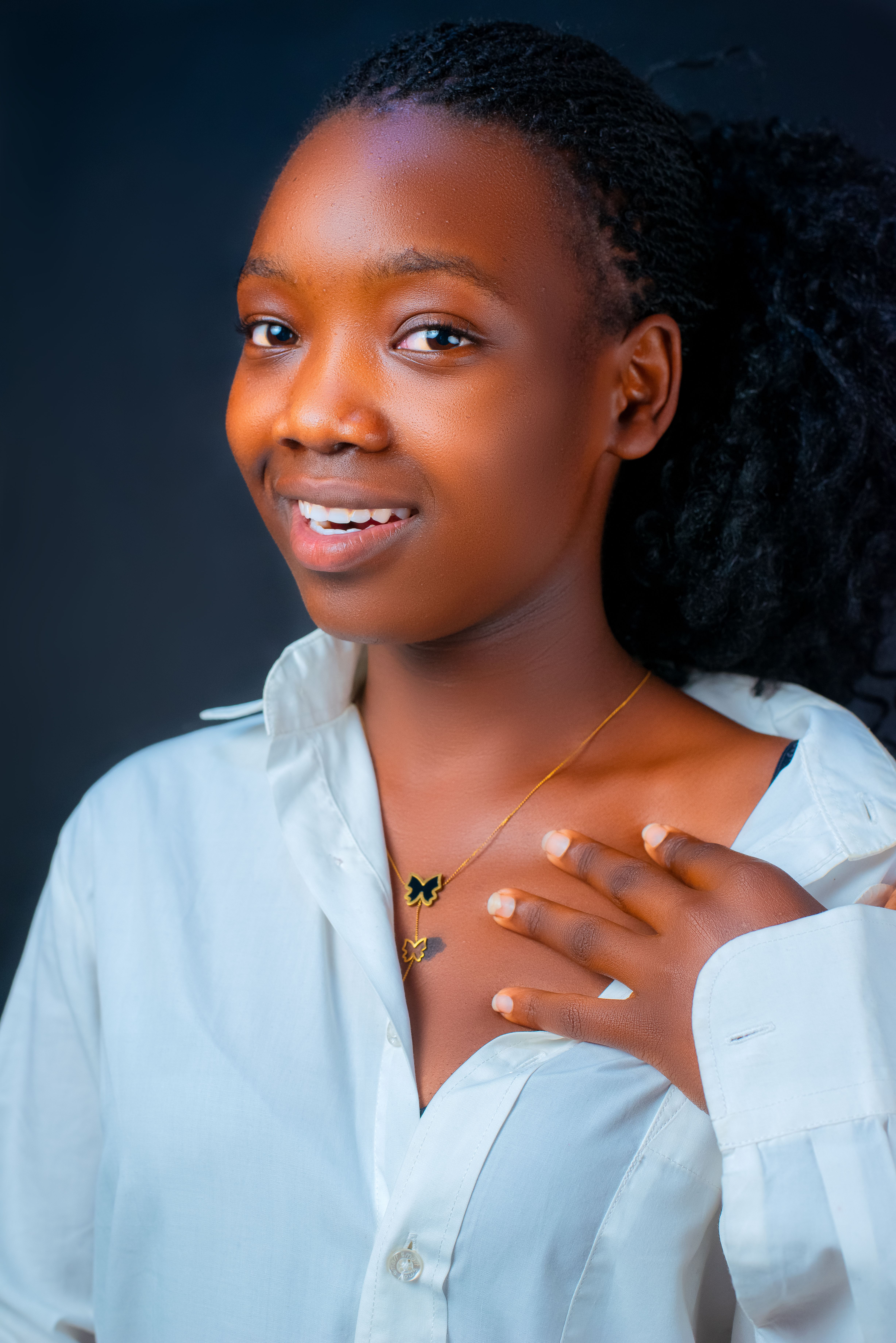 Portrait of a woman smiling, wearing a white shirt and butterfly necklace.