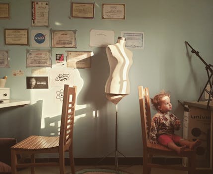 一个小孩坐在阳光明媚的房间里，椅子上方的墙上挂着一个人体模型和一些证书