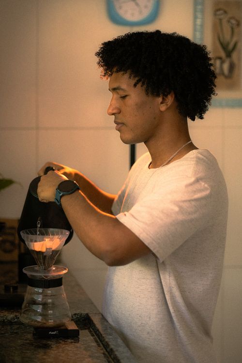 Free A young man attentively pours water into a pour-over coffee maker in a stylish kitchen. Stock Photo