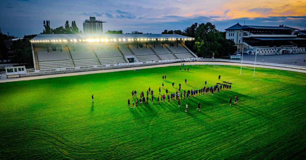 Aerial shot of a group practicing rugby under stadium lights at sunset, creating a vibrant and dynamic atmosphere.