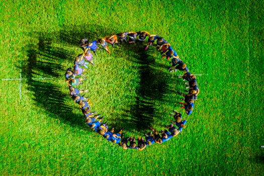 A diverse group of people forming a circle on a green field, viewed from above.
