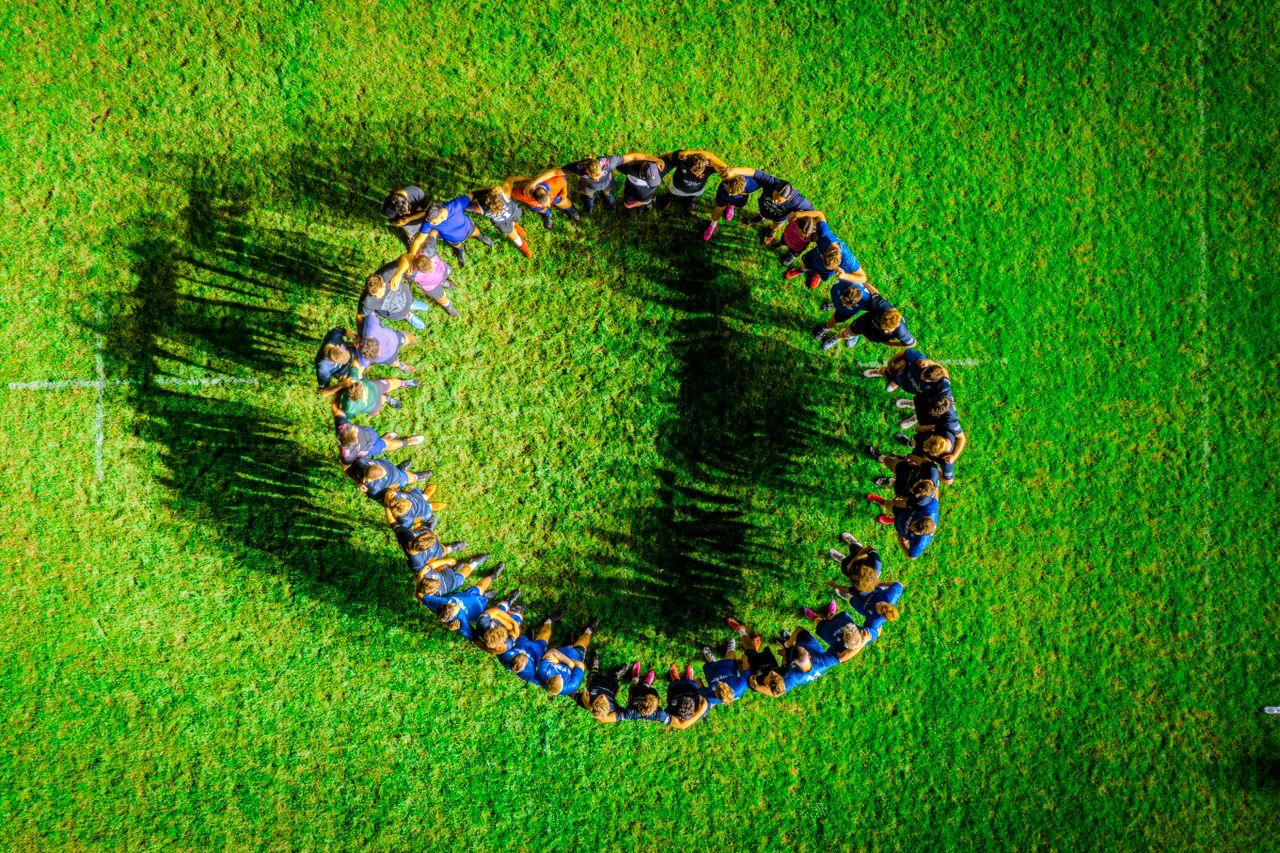 a diverse group of people forming a circle on a green field viewed fro
