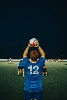 Rugby player in blue jersey preparing for lineout during a night game on an outdoor field.