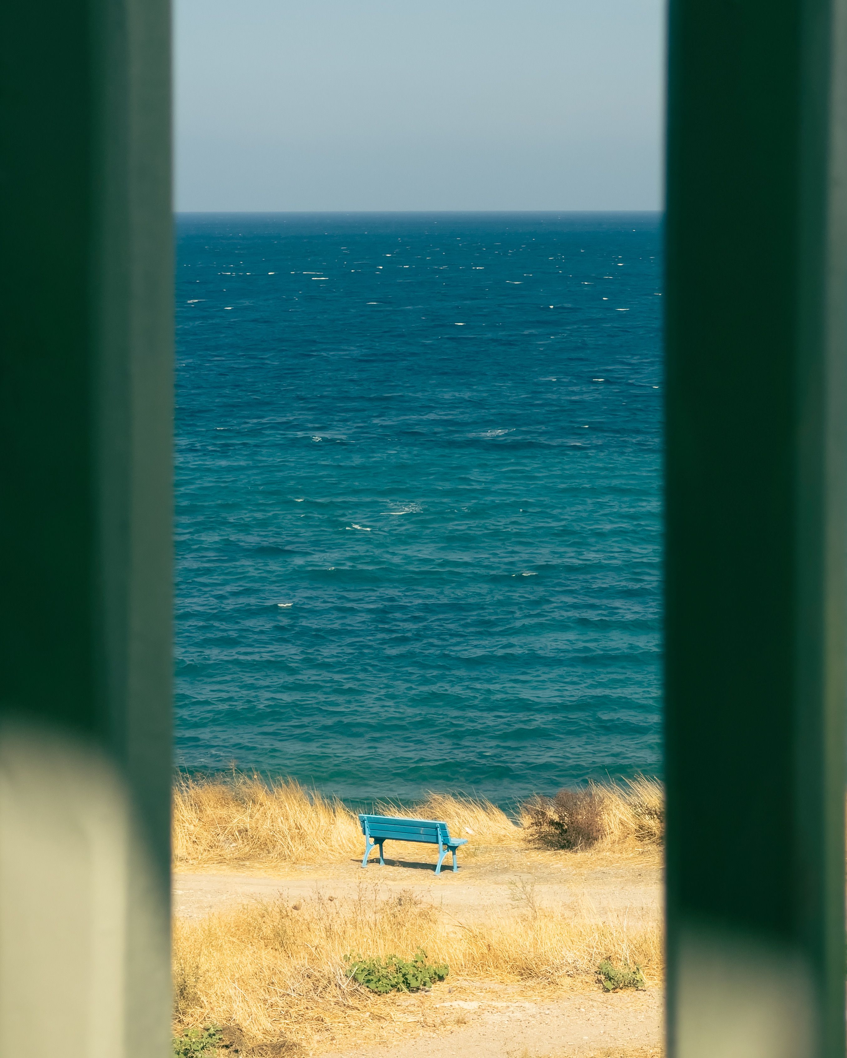 View of a serene ocean and bench through a coastal archway with golden grass.