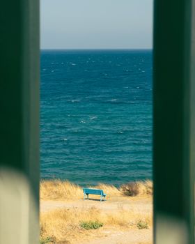 View of a serene ocean and bench through a coastal archway with golden grass.