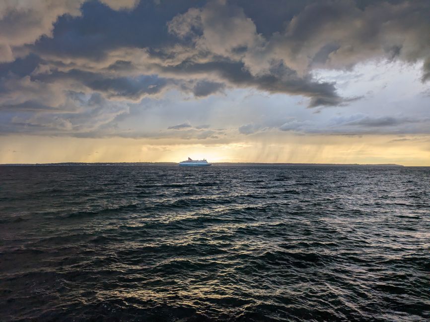 Cruise ship sails under stormy clouds at sunset over the ocean, creating a dramatic and serene scene.